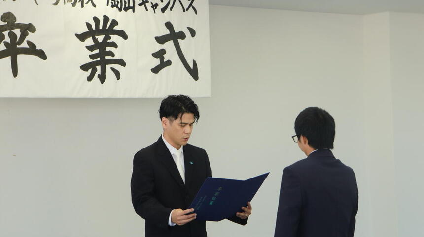 教室内でキャンパス長から卒業証書を受け取っている卒業生の写真