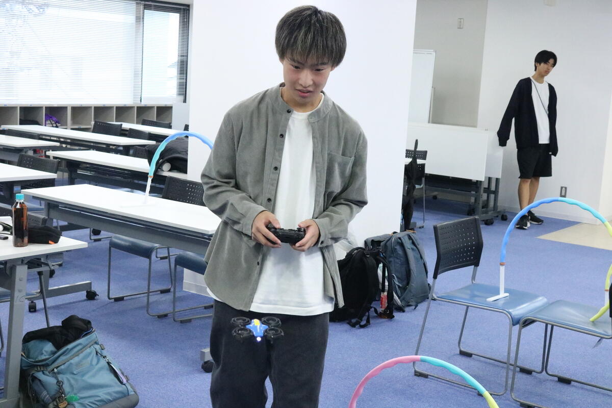 「みらいの架け橋レッスン®」の教室で生徒がドローンを操縦しフラフープをくぐらせている様子