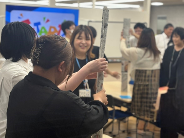 中学3年生と在校生がチームで協力し、声を掛け合いながら一番高い新聞紙タワーづくりに挑戦している様子。