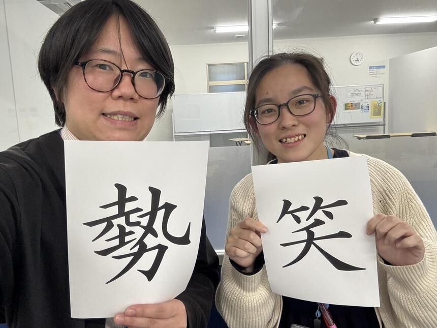自分で選んだ今年の漢字「勢」「笑」の紙を持って笑っている女性コーチ2名