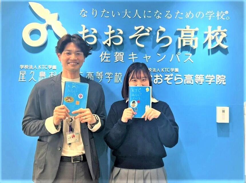 キャンパスのフロントサイン前でみらいノート®_0を持ったマイコーチと生徒