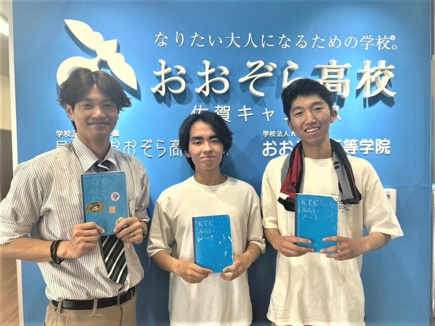 キャンパスのフロントサイン前でみらいノート®_0を持ったコーチと生徒2名