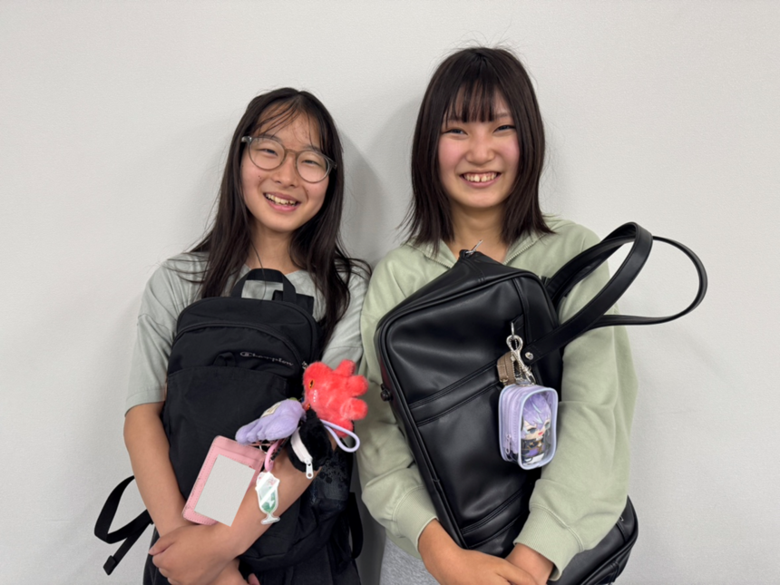 キャンパスで自分のカバンを抱き上げて、笑顔を見せる2人の女子生徒