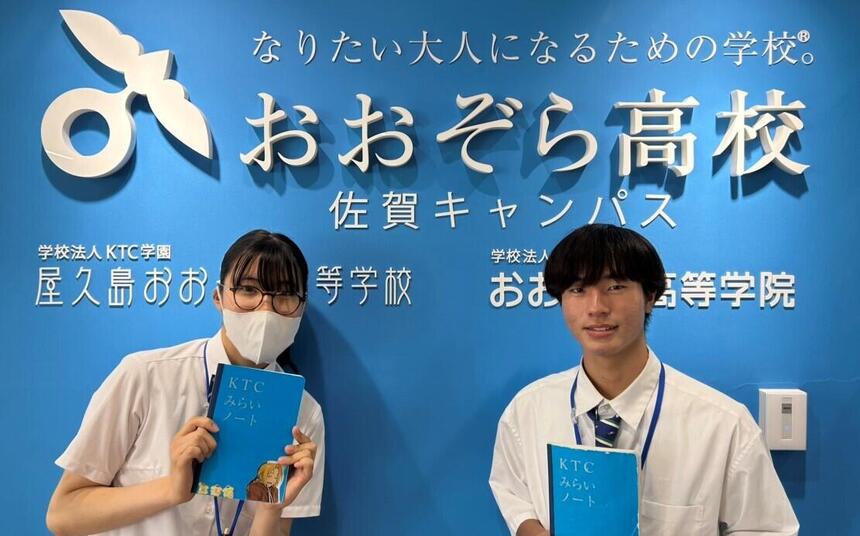 キャンパスのフロントサイン前でみらいノート®を持った生徒2名