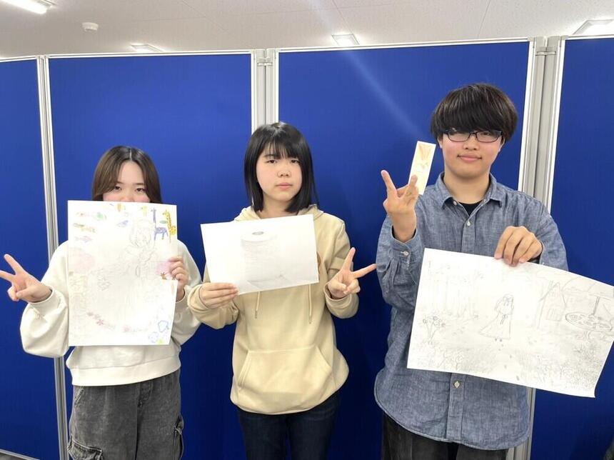 3人の高校生が自作のイラストの作品を持ちながら笑顔でうつっている写真