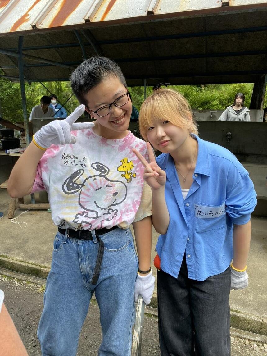 女子生徒2人が火起こし中に笑顔でピースをしている様子