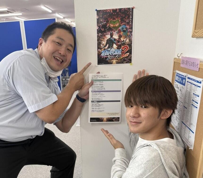 堺キャンパスにて、生徒企画のチラシを示しながら、生徒とコーチがカメラに目線を送っている様子