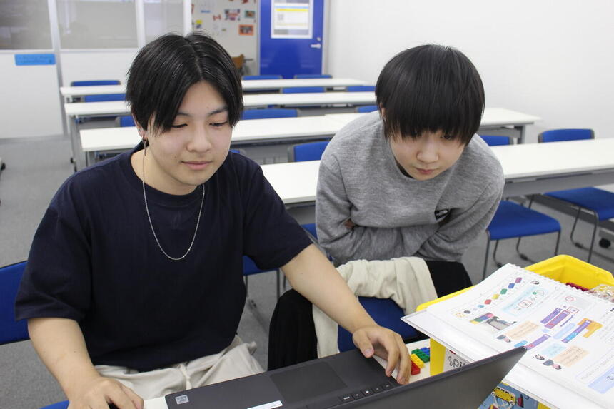 プログラミングコースでコース生同士がパソコンを一緒に見ながらプログラムについて教え合っている様子