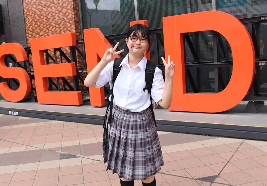 1年次女子生徒が、仙台駅前の「SENDAI」ロゴ前で笑顔で写真に写る様子。