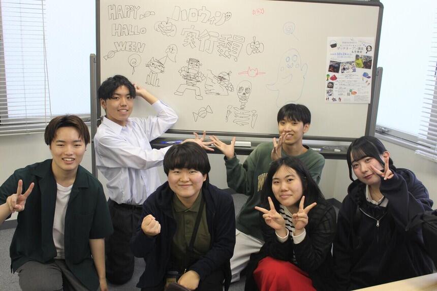 実行委員の生徒が、ホワイトボードの前で笑顔で写真にうつる様子。
