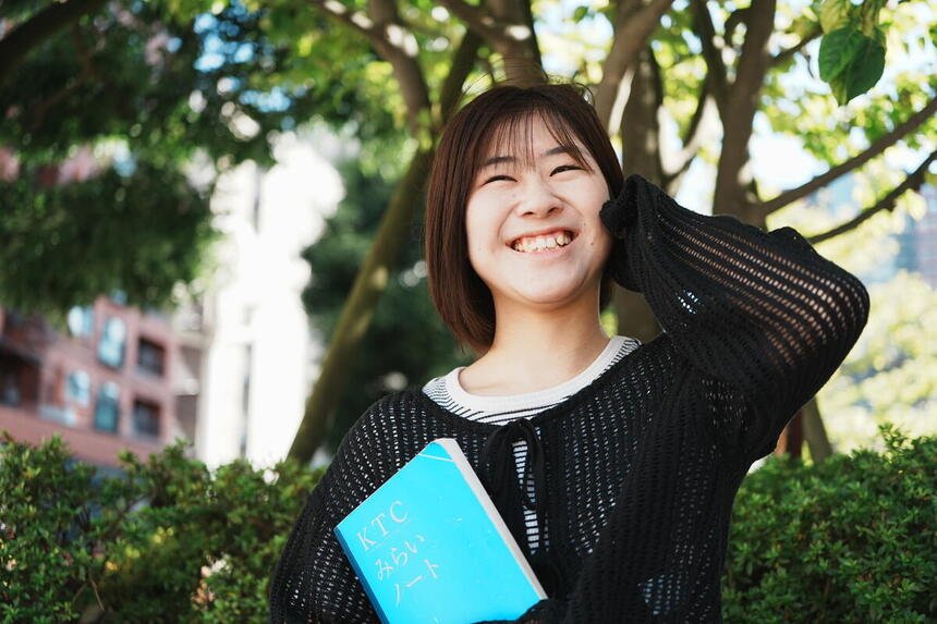 屋外で転入学してきた女子生徒がみらいノート®を持って笑顔で写真に写っている様子。