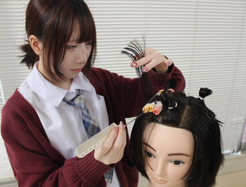 専門学校コラボのみらいの架け橋レッスンで、生徒が真剣な表情でパーマ用のロッドを巻き付けるワインディング体験に取り組んでいる様子