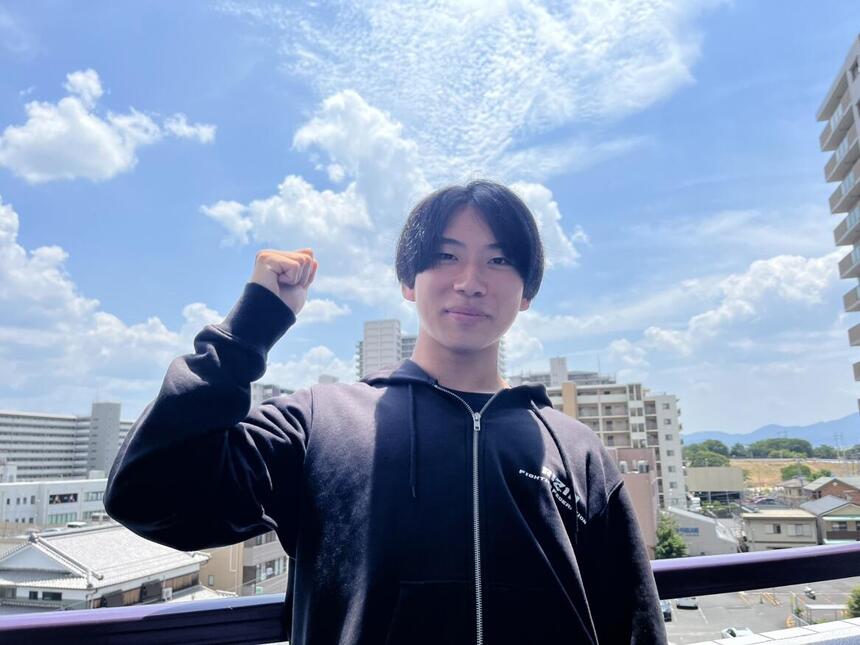 青空を背景にキャンパスでガッツポーズをしている男子生徒
