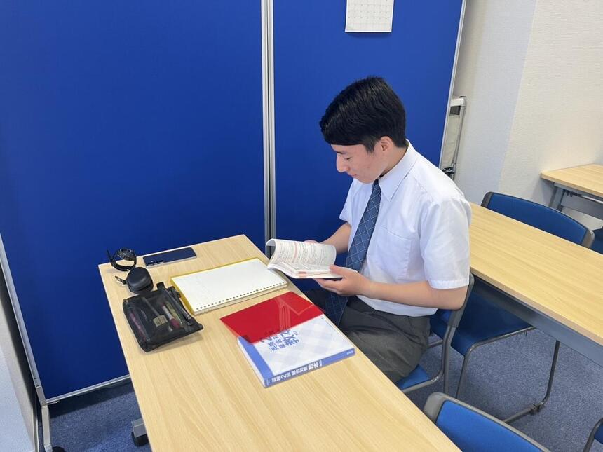キャンパスの教室で英語の問題集を開きながら勉強する男子生徒