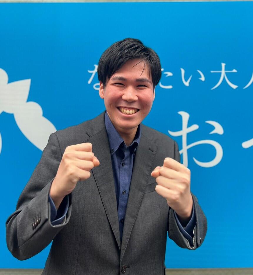 一人の男性が両腕のこぶしを胸の前に挙げ、笑顔で写っている写真