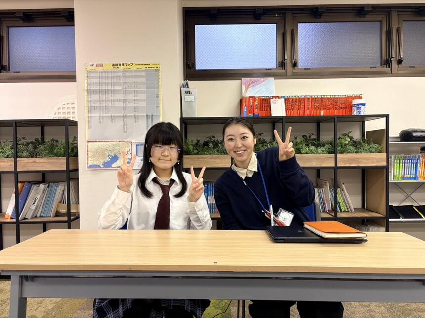 コーチと生徒が椅子に座り、笑顔でピースをしている写真