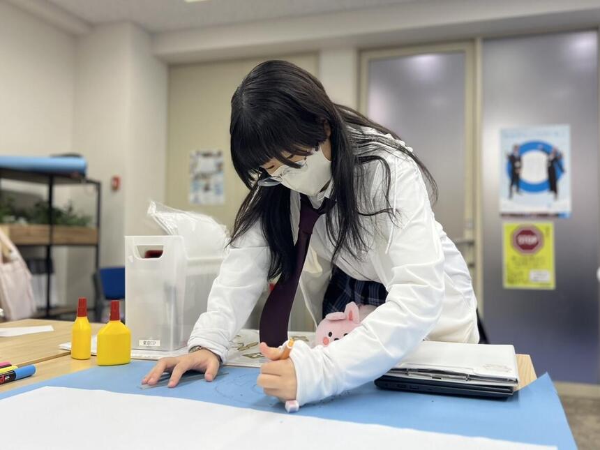 女子生徒が真剣な表情で模造紙を作成している様子