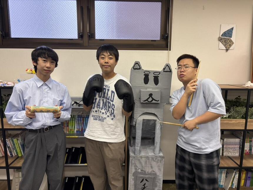 男子生徒3名が、モルックのスキットル、ボクシンググローブ、ドラムスティックを手にポーズをとっている。