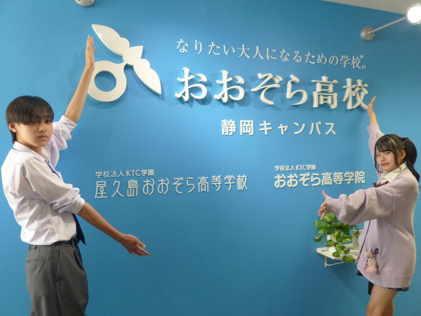 静岡キャンパスの入り口で男女が看板を強調している姿