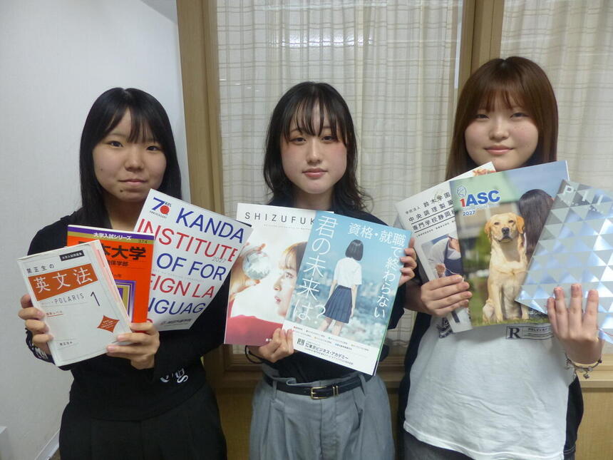 教室で大学などのパンフレットを持っている3人の生徒の写真