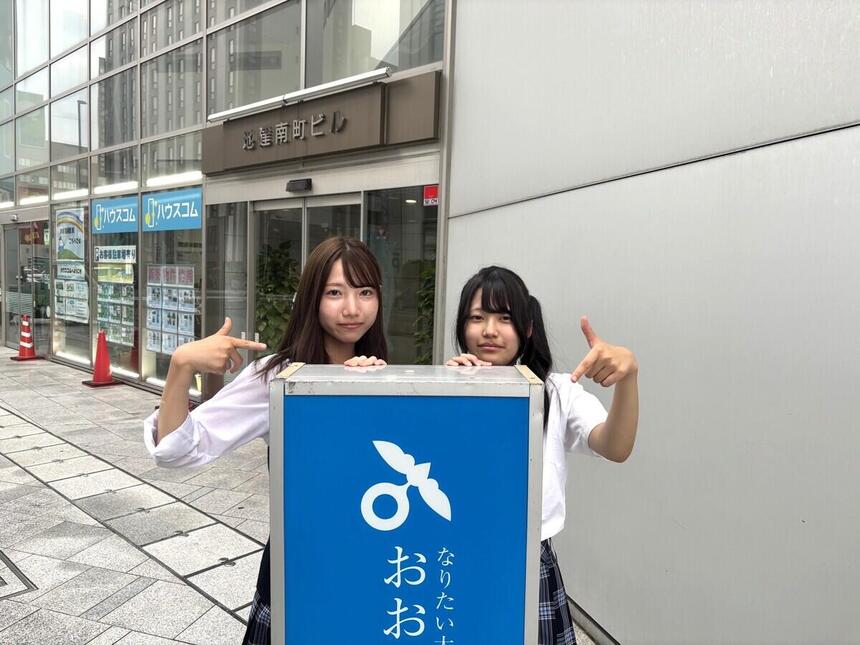 生徒がキャンパスのビルの前で看板を指さしている写真。