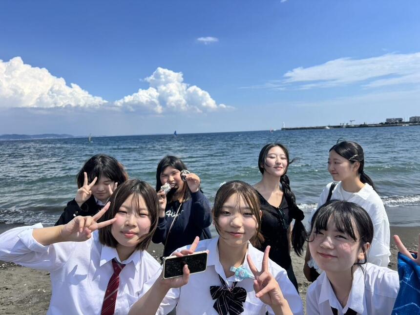 江ノ島の海辺にて、おおぞらをバックにポーズを決めている笑顔の生徒