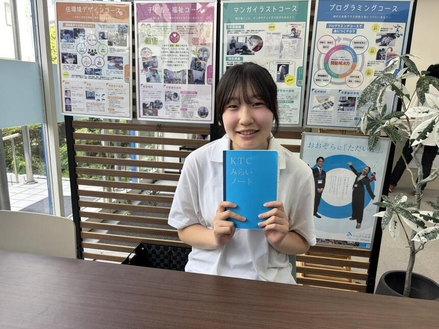 キャンパスエントランスの面談ブースにて、KTCみらいノート®を掲げた笑顔の生徒