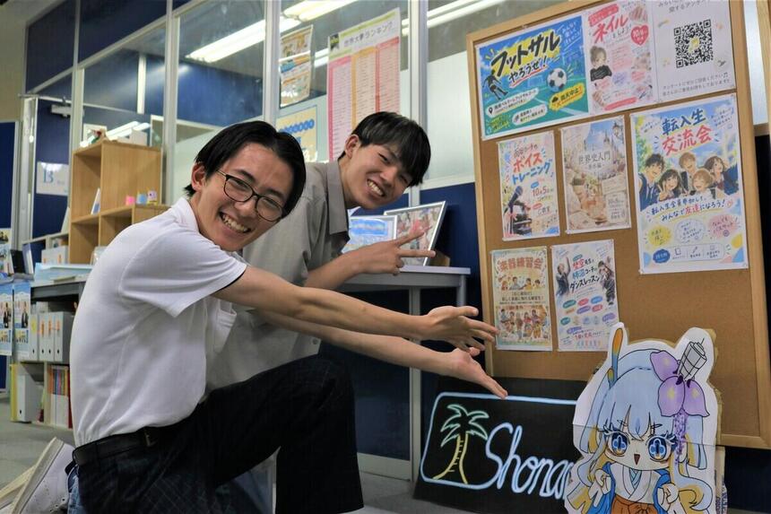 湘南キャンパス内に設置した新しい掲示板の前でポーズをとる笑顔の生徒