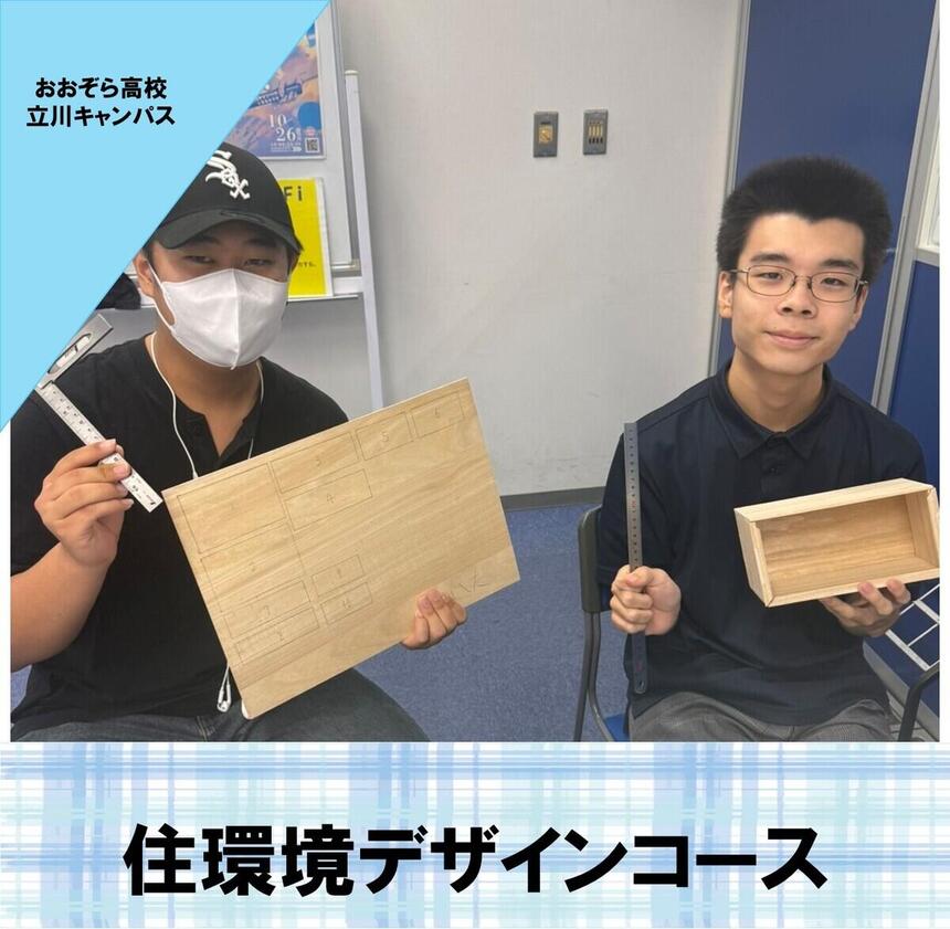 住環境デザインコースの生徒が立川キャンパスの教室で木材を持って笑顔で座っている写真