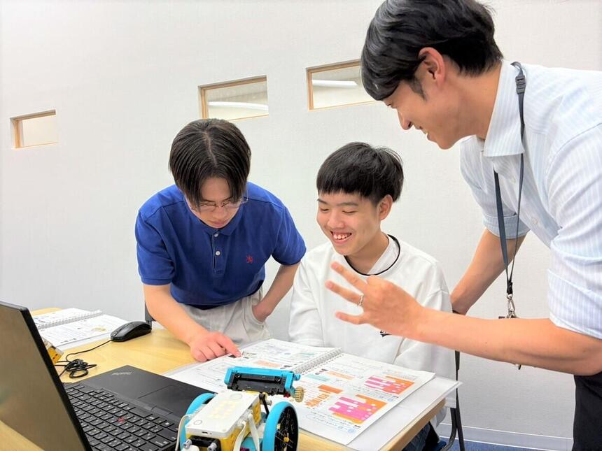 1年生にプログラミングを教えている2年生とマイコーチ®がいいねをしている様子の写真