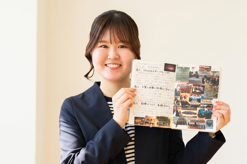 高崎キャンパスの中で、思い出の写真やメッセージが書かれたKTCみらいノート®を広げて見せてくれる笑顔の清水コーチ