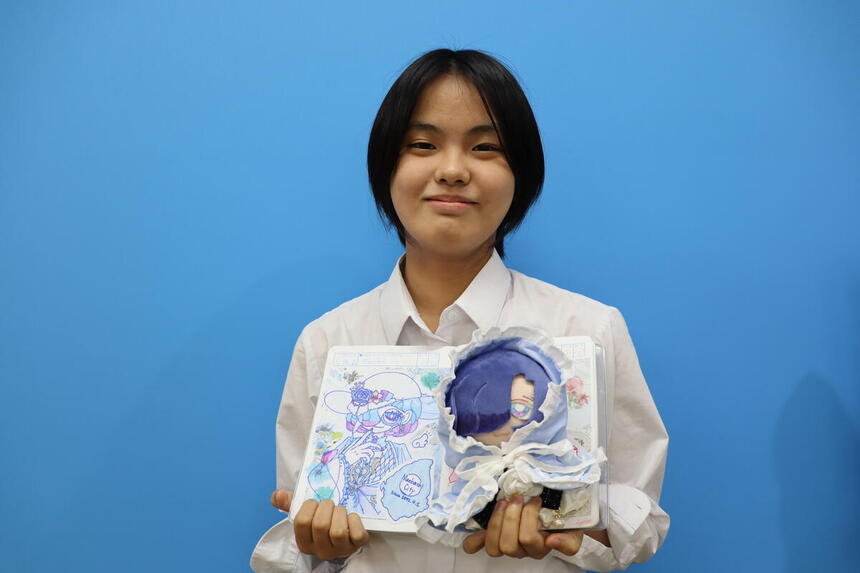 高崎キャンパスの女子生徒が、自分で手作りした前橋市をイメージしたぬいぐるみを笑顔で持っている写真