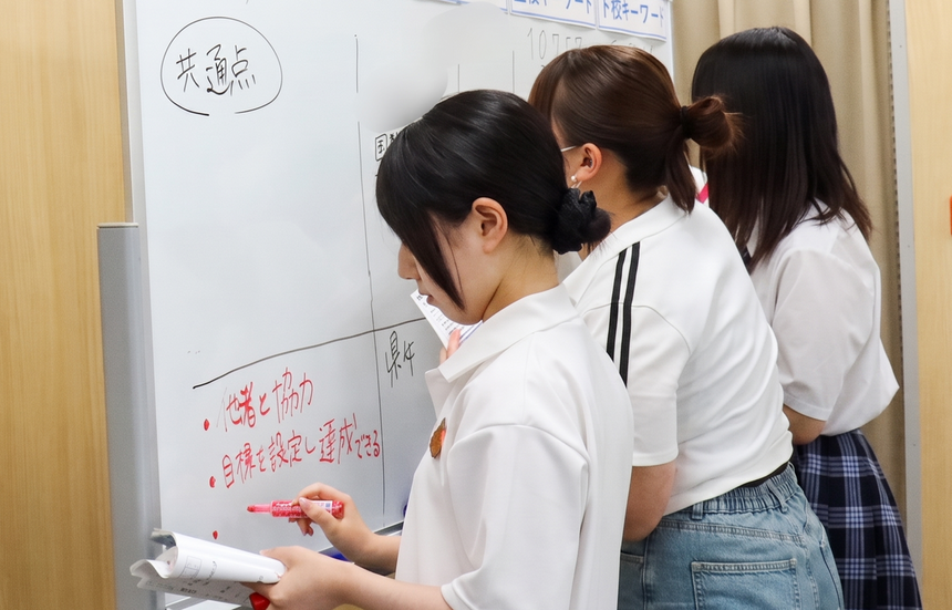 みらいの架け橋レッスン®の進路講座で、高崎キャンパスの生徒たちがホワイトボードに書かれた看護学部のアドミッションポリシーの分析結果を見ながら、笑顔で意見を出し合って比較・整理している様子。