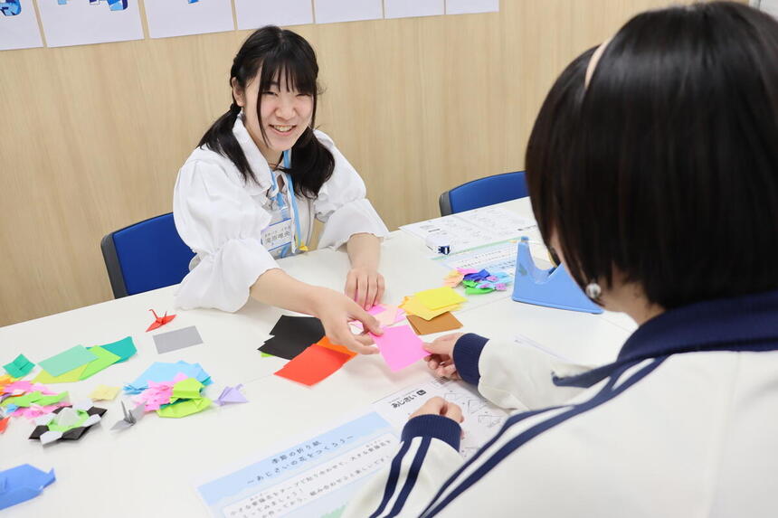 6月27日(土)高崎キャンパスの体験入学で、在校生の先輩が中学生に折り紙の折り方を優しく教えている様子