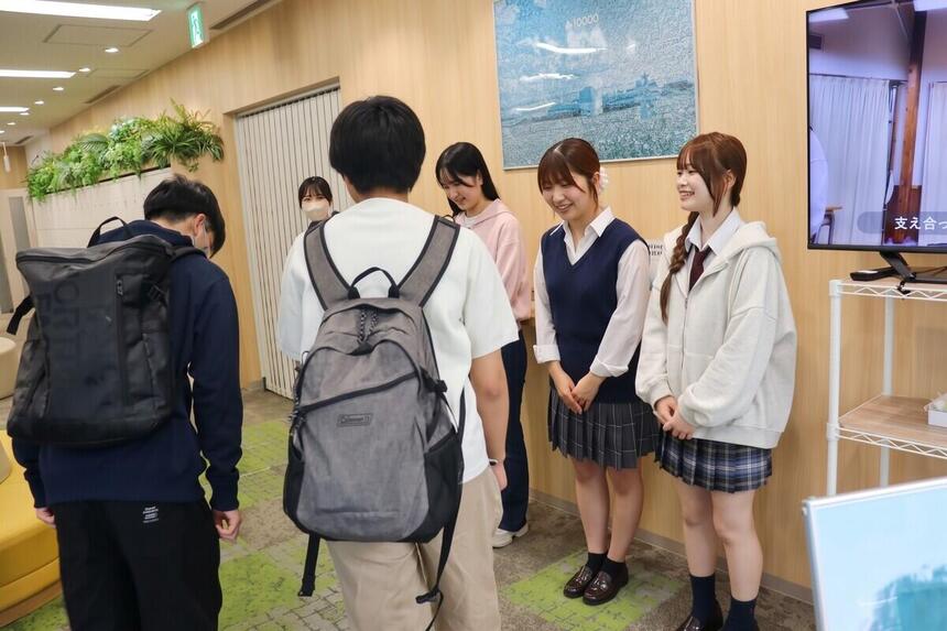 高崎キャンパスのエントランスで、登校してきた生徒に笑顔で頭を下げて挨拶を交わす生徒とコーチの様子