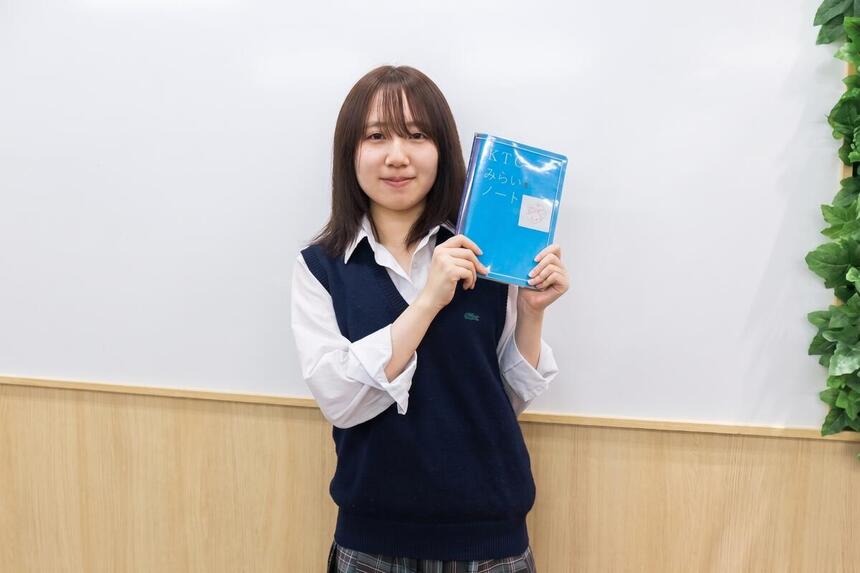 高崎キャンパスの教室で、3年生の女子生徒がKTCみらいノート®を両手で持って進路報告をしている様子