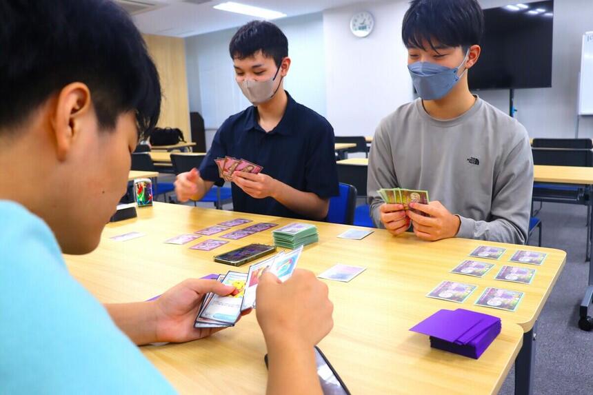 高崎キャンパスの机で3人の男子生徒がトレーディングカードゲームを楽しんでいる様子