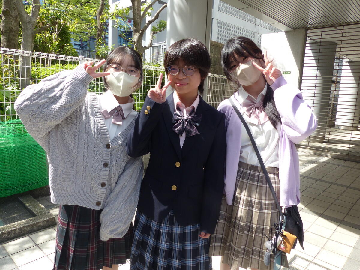 3人の1年次生が制服を着てキャンパスの前で笑顔で写っている写真