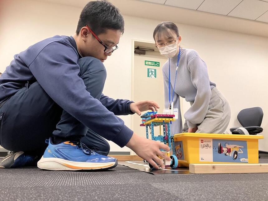 ロボットを調整する生徒を、コーチが見守ります。