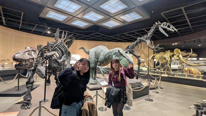 博物館で、恐竜をバックに生徒が真似をしてポーズをとっています。