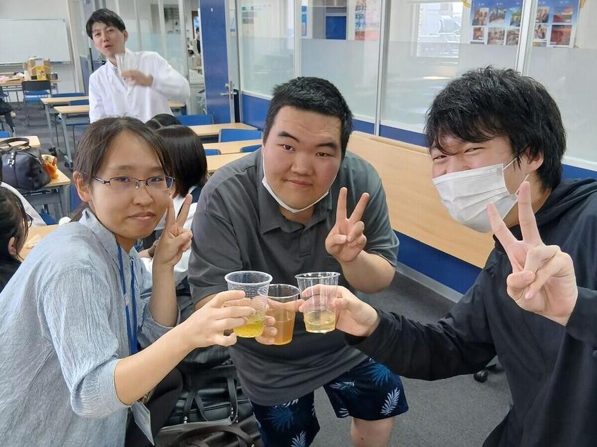 生徒とコーチが笑顔でクラフトコーラを手にして乾杯している様子