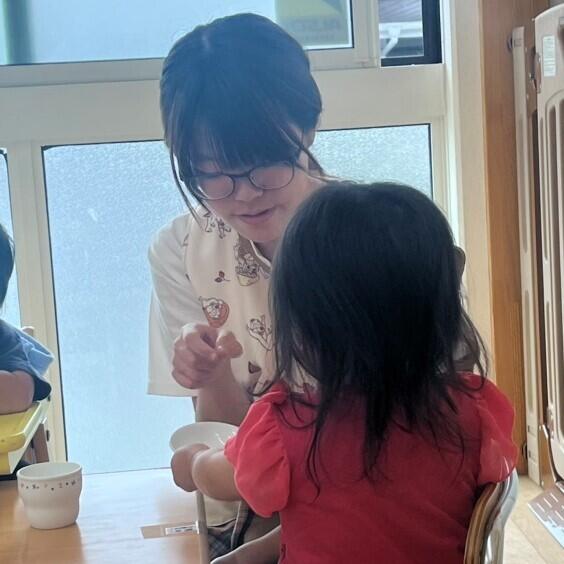 実習先の保育園で、おやつを食べている園児に生徒が話しかけています。
