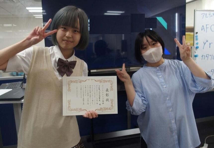 生徒がキャンパスで行われた音楽クイズに優勝し賞状を持って記念写真を撮っています。