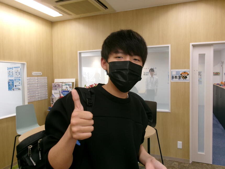 インタビューを受けた1年次男子生徒の写真。和歌山キャンパスの教室内でグッドポーズを取っている。