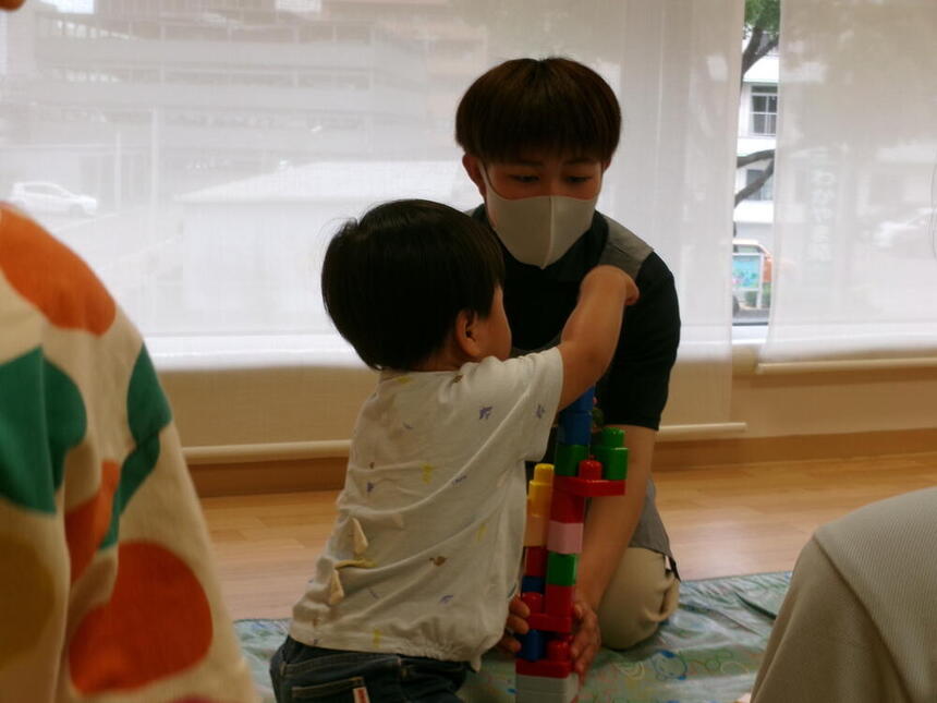 実習先の保育園にて、子ども・福祉コースの生徒が、1歳児の園児と一緒にブロックで遊んでいる様子。