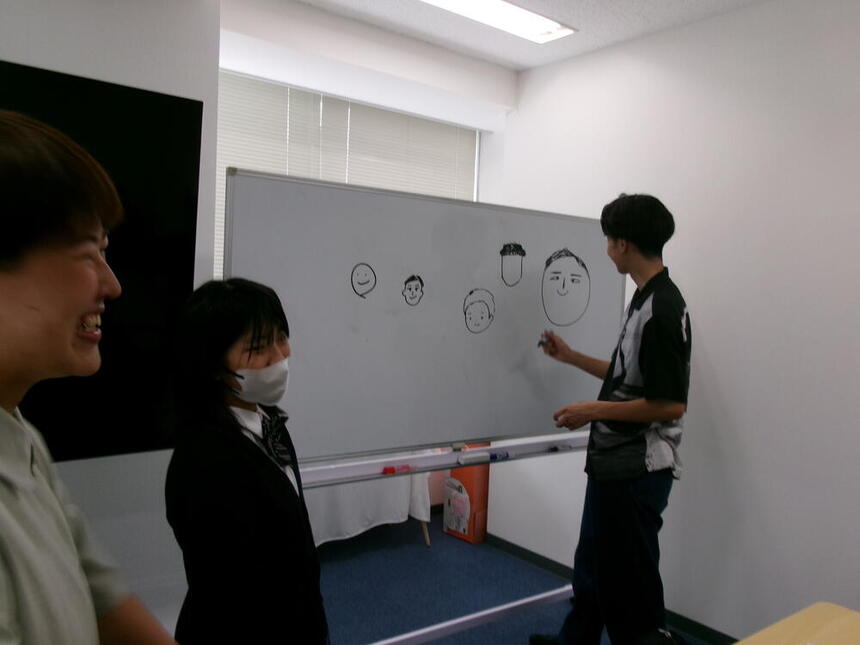 昼休みに3学年が集まってホワイトボードにコーチの似顔絵を書いている様子。