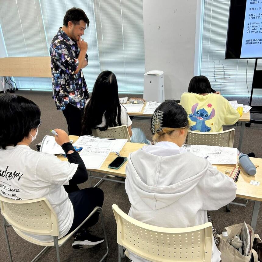マンガ塾の講師が生徒のイラストを見ている様子、生徒4名がイラストを描いている