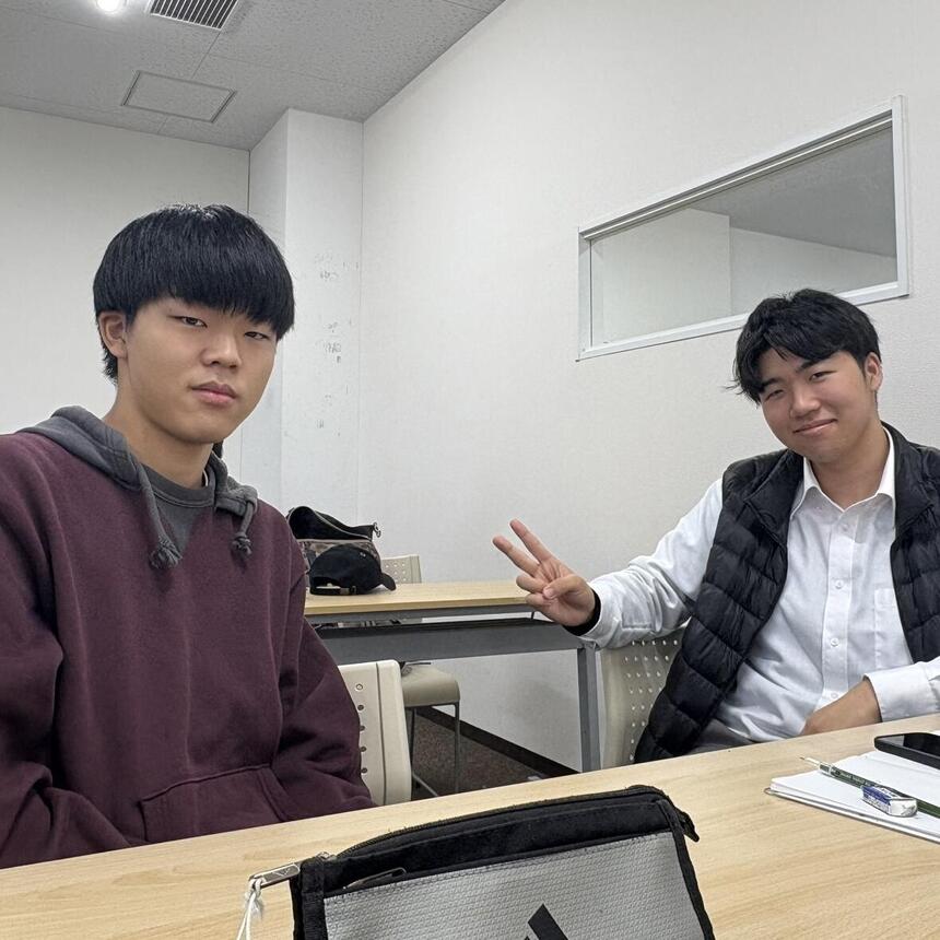 生徒二人が椅子に座っている。右の男子生徒はピースをしている。