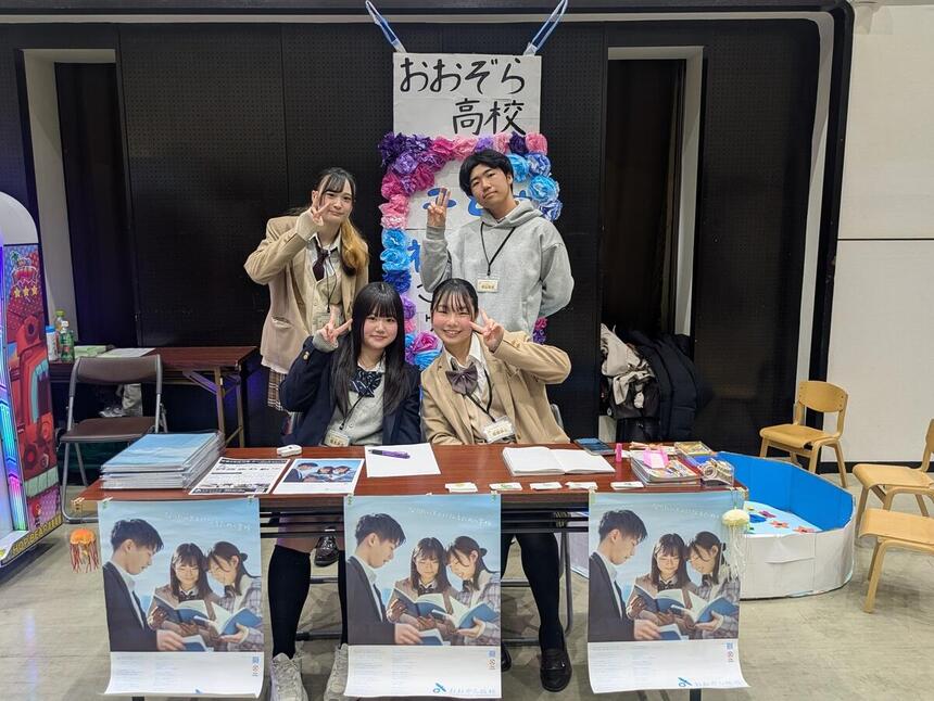 おおぞら高校の看板の前でピースをする4人の生徒。