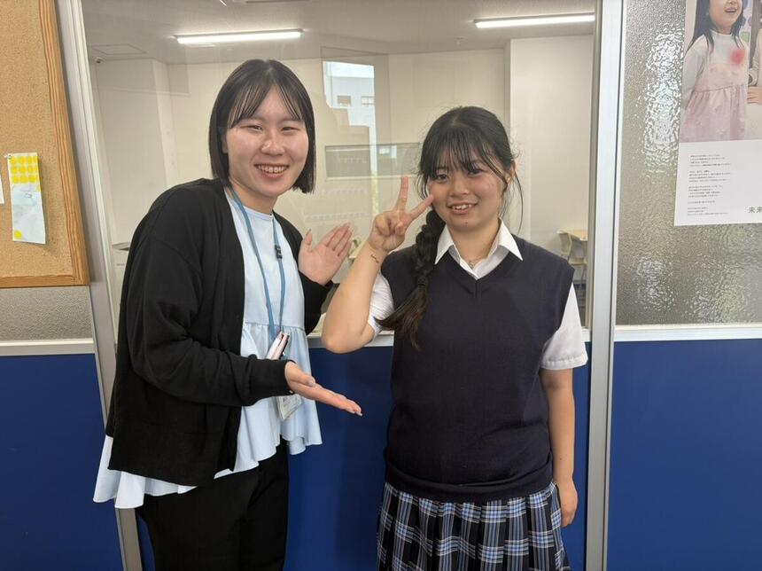 教室の前で笑顔を浮かべる生徒とコーチの写真